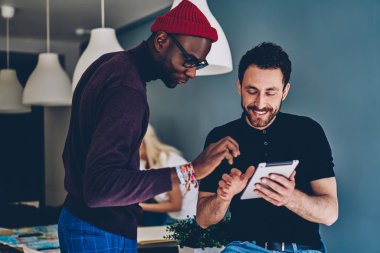 Afrikalı-Amerikalı genç adam kablosuz 4 g kullanarak modern Dokunmatik ped cihaz üzerinde app yüklemek için beyaz arkadaş yardım internet. İki arkadaşları dijital tablet Web sitesinde bilgi okuma