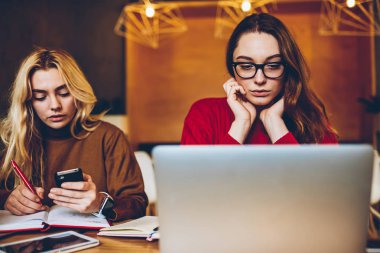 Düşünceli kız öğrenci eğitim yoluyla becerikli, sınav için dizüstü bilgisayar bilgi arkadaşı içinde Not yazma sırasında elde eğitsel izlerken ciddi genç kadın hazırlanıyor konsantre