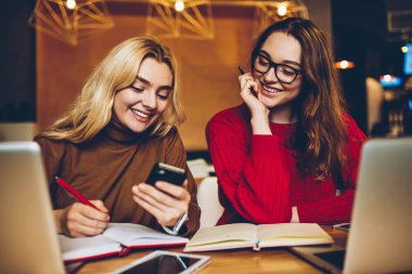 Eğleniyor neşeli kız öğrencilerin öğrenme alanı birlikte coworking Smartphone fotoğraflarına bakmaktan, komik video gülmek gülümseyen hippi kız uzaktan cooperatin çalışan cep telefonu üzerinde göz