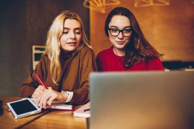 Zeki kız öğrencilerin birlikte webinar dizüstü bilgisayar, Netbook Cafe Interio ağlarından bilgi okuma kurs için fikirler tartışırken hipster kızlar izlerken ödev