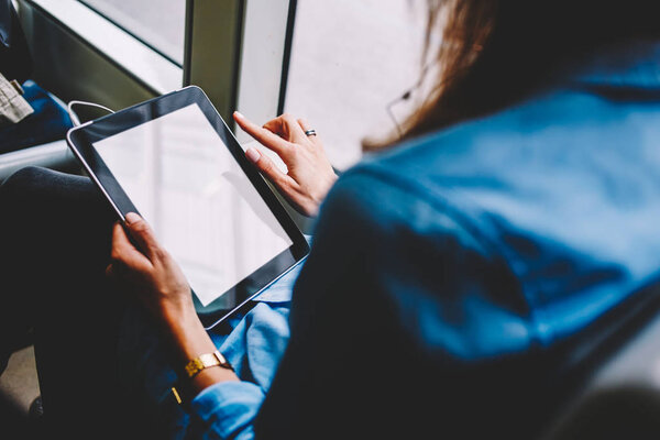 Cropped back view of female person holding modern touch pad device with copy space display for your website content.Young woman with tablet in hands using public transport wireless internet in tram