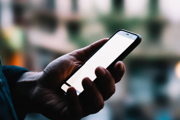 Боковым крупным планом видно, как мужчина держит в руках современный смартфон с макетом экрана для копирования, стоя на фоне бокса. Человек, использующий приложения для мобильных телефонов с подключением к Интернету
