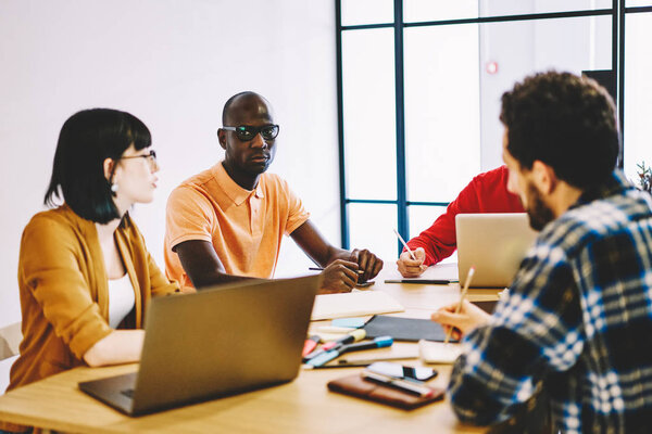 Multicultural group of young people dressed in smart casual wear discussing plan of collaboration having briefing meeting in office.Diverse students teamworking on design project during brainstorming