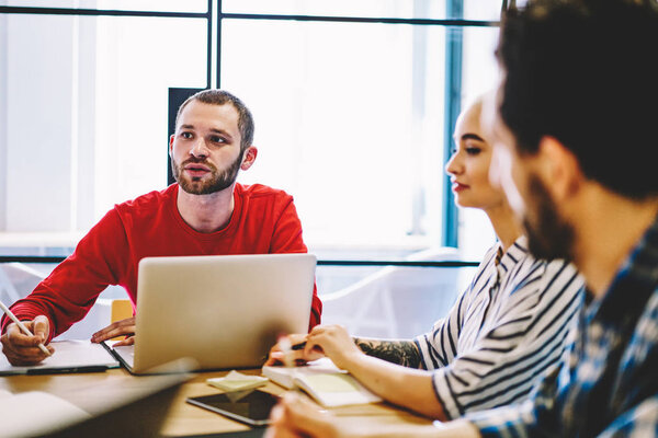 Group of young people dressed in smart casual wear discussing working plan of collaboration sitting at meeting table in office.Team of creative employees talking about productive strategy of project