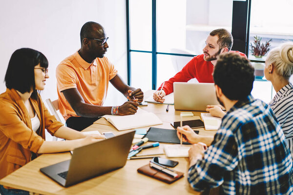 Multicultural group of young people dressed in smart casual wear discussing planning strategy having brainstorming meeting in office.Diverse employees collaborating on organization of working process