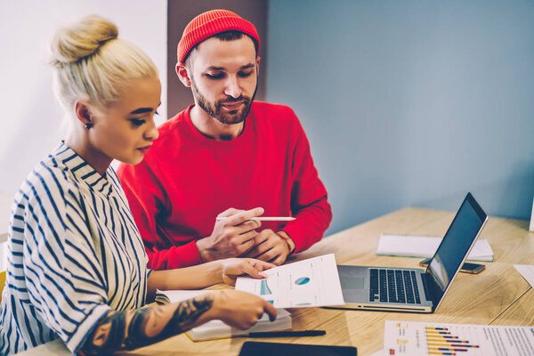 Two colleagues discussing graphic collaborating on illustration sitting at desktop with laptop computer in office.Hipster male tutor explaining sketch to student during private lesson in coworking