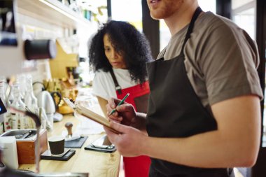 Çok kültürlü baristas mali rapor, kendi iş başlangıç yapmak için birlikte çalışmaya görünümünü kırpılmış. Plan maliyet kontrol önlük iki erkek ve kadın işçiler ayakta adlı bar-kendi Cafe