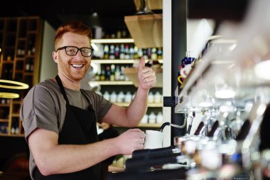 Profesyonel barista fotoğraf makinesi ile parmak kadar kahve içecek modern makine üzerinde istemci için hazırlarken gülümseyen çalışma müreffeh genç adam portresi. Olumlu erkek garson işaret gösteren ok