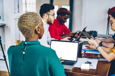 Çok kültürlü bir grup genç insan ofiste dizüstü bilgisayar boş ekran alanı ile Internet içeriği kullanarak beyin fırtınası sırasında işbirliği proje planını tartışıyor akıllı rahat kıyafet giymiş