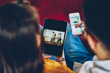 Genç kadının hipster adam akıllı posta kontrol ederken modern dokunmatik yüzey üzerinde online alışveriş yaparken arkadan görünüm kırpılmış. Kaç tablet cihaz üzerinde görüş fotoğraf ve telefon üzerinde medya paylaşma aşk içinde