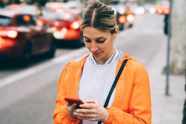 Genç erkek şehir sokak üzerinde duran cep telefonu veri Internet bağlantısı kullanarak görünümünü kapatın. Taksi çağıran beyaz hippi kız turuncu ceket manifatura iletide smartphone uygulama,