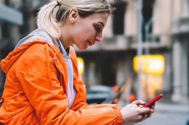 Genç erkek şehir sokak üzerinde duran cep telefonu veri Internet bağlantısı kullanarak görünümünü kapatın. Metin mesajı ile sohbet etmek kullanma Smartphone cep telefonu ile okuma turuncu ceketli beyaz hippi kız