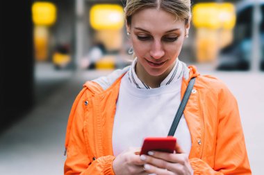Genç erkek şehir sokak üzerinde duran cep telefonu veri Internet bağlantısı kullanarak görünümünü kapatın. Metin mesajı ile sohbet etmek kullanma Smartphone cep telefonu ile okuma turuncu ceketli beyaz hippi kız