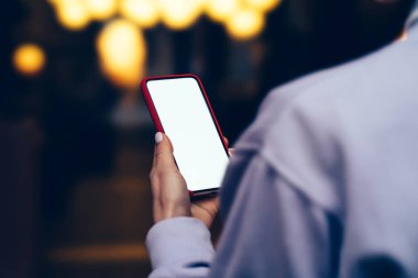 Omuz kadın kişinin parmak kopyalama alanı ekranı modern smartphone bokeh ışıklar arka plan açık havada duran ile dokunmadan görünümünden arka. Cep telefonu uygulamaları ile internet kullanan kadın