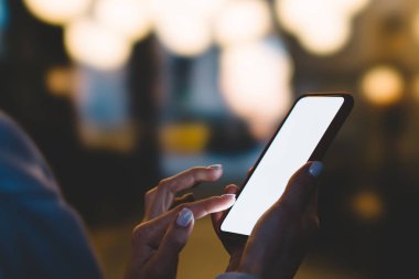 Yan kadın kişi ile parmak kopya alanı perde modern smartphone duran gece bokeh ışıklar arka plan açık havada, dokunmadan görünümünü kapatın. Cep telefonu uygulamaları ile internet kullanan kadın