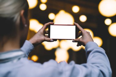 Arkadan Görünüş kadın tutun yatay konum cep telefonu altın shinning bokeh ışıklar karşı elinde zaman akşam. Kadın modern smartphone ile boş mockup kopya alanı perde reklam için tutar