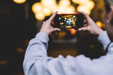 Arkadan Görünüş kadın ile yatay konum cep telefonu elinde tutan ve yüksek kaliteli dijital fotoğraf makinesinde altın shinning ışıklar fotoğraf çekme. Ekrandaki görüntü ile Smartphone cep telefonu ile kadın alarak resim