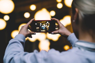 Arkadan Görünüş kadın ile yatay konum cep telefonu elinde tutan ve yüksek kaliteli dijital fotoğraf makinesinde altın shinning ışıklar fotoğraf çekme. Ekrandaki görüntü ile Smartphone cep telefonu ile kadın alarak resim