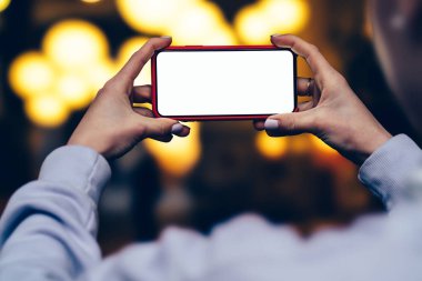 Arkadan Görünüş kadın tutun yatay konum cep telefonu altın shinning bokeh ışıklar karşı elinde zaman akşam. Kadın modern smartphone ile boş mockup kopya alanı perde reklam için tutar