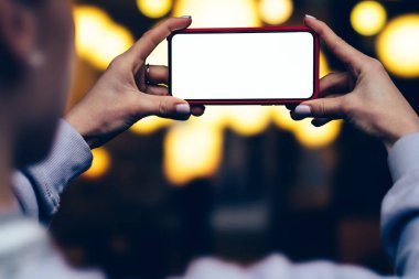 Kadın arkadan görünüm tutun yatay konum cep telefonu altın shinning bokeh ışıklar karşı elinde zaman akşam. Kadın modern smartphone ile boş mockup kopya alanı perde reklam için tutar