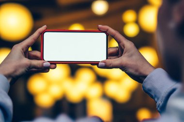 Kadın arkadan görünüm tutun yatay konum cep telefonu altın shinning bokeh ışıklar karşı elinde zaman akşam. Kadın modern smartphone ile boş mockup kopya alanı perde reklam için tutar
