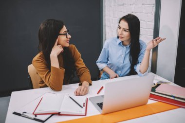 İş üzerinde işbirliği planlama ödev görev sınıf için dizüstü bilgisayar tartışırken fikirler ile masada oturan kadın öğrencilerin iş hakkında konuşmayı yetenekli kadın arkadaşları