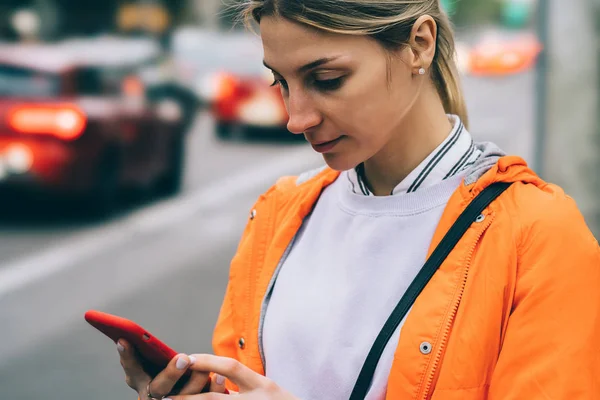 若い女性の街に立っている間携帯電話データ インターネット接続のビューを閉じます タクシーを呼び出すスマート フォン アプリケーションで オレンジ色のジャケット テキスト メッセージで白人の内気な少女 — ストック写真