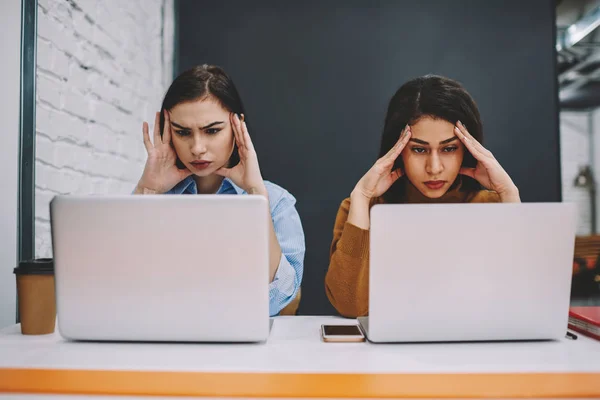 Sad frustrated girls feeling heachache while preparing for exams in campus using laptop computers, unhappy antisocial women tired and bored during working process completing project before deadline