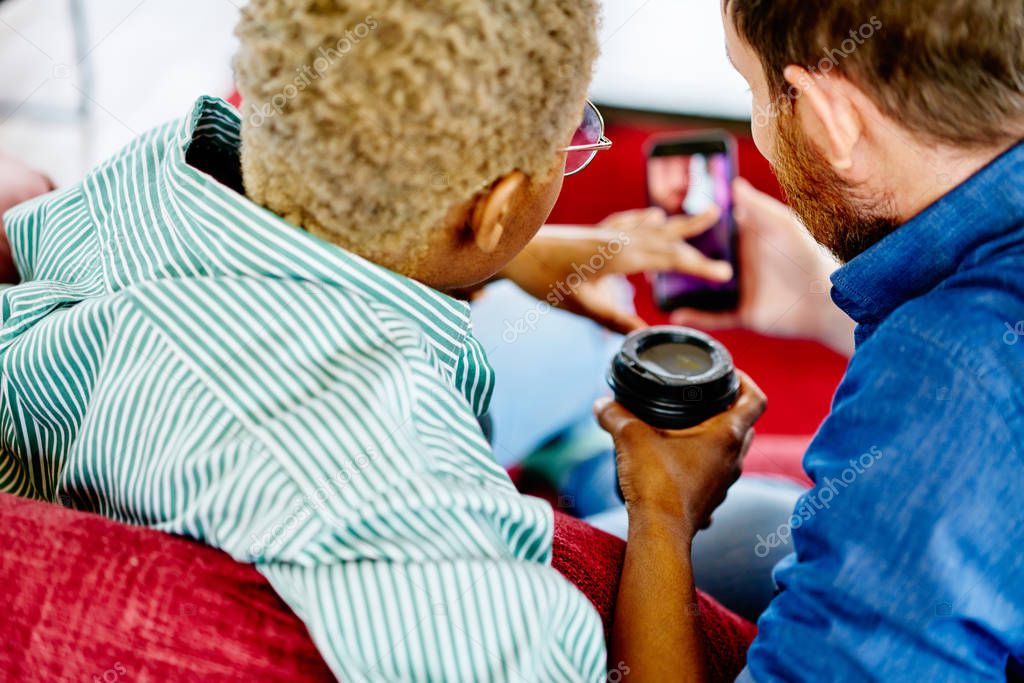 Cropped image of diverse young people choosing app on website to install on digital smartphone using 4G internet.Back view of two friends watching video online in social networks on mobile phone