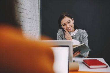 Büyüleyici neşeli esmer kişinin iletişim yarım uzunluk portre görünümü görüntü müreffeh yetenekli çalışanın cep üzerinde çalışmaları sırasında konuşurken geri kapalı, smartphone uygulama kullanarak