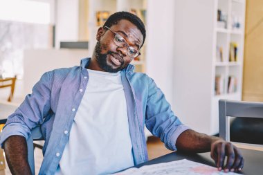 Masaüstü alanı, coworking içinde oturan ev ödevi görevi yapmaya konsantre genç Afro-Amerikan hipster adam şaşkın akıllı koyu tenli erkek fikir makale üzerinde durulması onun Not defteri bakarak