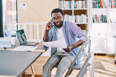 Kağıtları bilgilerle tutan telefon konuşmayı ciddi Afrikalı-Amerikalı işadamı portresi, Genç karanlık erkek yapım hizmeti işleci ile danışmanlık için telefon derili.