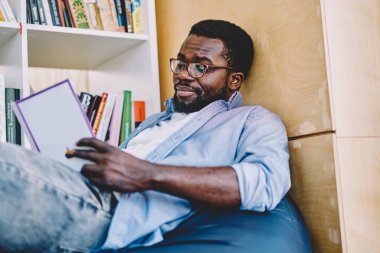 Dalgın Afro-Amerikan zeki adam ilginç bestseller üzerinde konsantre sırasında serbest zaman, düşünceli koyu tenli öğrenci vakit otodidakt okuma ve çözümleme kitap kolej kütüphane