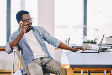 Cep telefonu konuşmayı Masaüstü, koyu tenli hipster adama iş dizüstü compute müşteri destek servisi güncelleştirme yazılımı için çağrıda oturan genç Afro-Amerikan serbest meslek