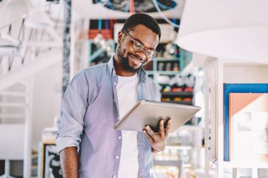 Sosyal ağlar, yeni veri kaynakları hakkında Başlarken bildirim Afro-Amerikan blogger online iş alanı coworking içinde dijital tablet kullanma memnun gülümseyen Eyewear genç adam olumlu koyu derili