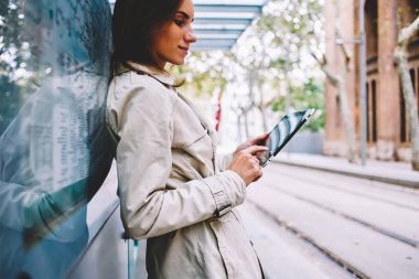 Şık genç kadın yan görünüm dijital tablet 4 g internet duran tramvay durağı kentsel ortamda bağlı metin yazmaya trendy ceket giymiş. Kadın blogger bildirim dokunmatik yüzey üzerinde okuma