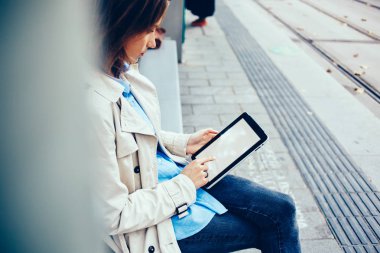 Genç kadın sahte yukarıya göstermek 4 g internet bağlantısı online alışveriş yaparken modern tablet üzerinde parmak ile dokunmadan yan görünüm. Şık erkek tramvay durağı üzerinde oturan Dokunmatik ped cihaz üzerinde metin yazma