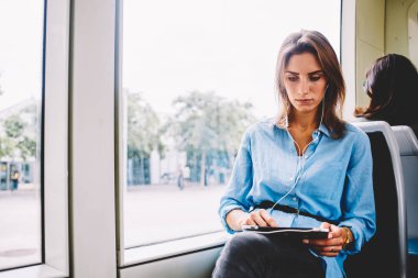 Tramvayda oturan pad aygıt dokunmak bağlı kulaklık Web sitesinde ses oyuncu online dinleme dalgın genç kadın. Hipster blogger video izlemek tablet ile ücretsiz kablosuz internet taşıma