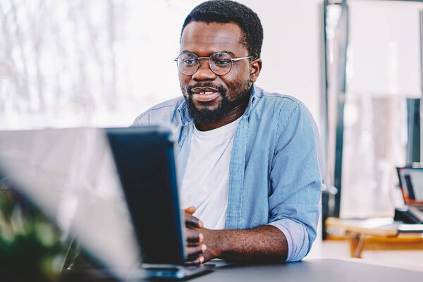 Smart african american dark skinned man watching tutorial on laptop computer wear eyeglasses for vision protection, dark skinned millennial guy satisfied with wifi connection enjoying movie onlin
