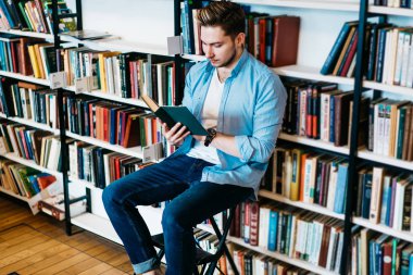Favori edebiyat kitap elinde tutan ve hobi genel Kitabevi kitaplığı boş zaman harcama dalgın hipster adam. Akıllı genç adam bestseller okuma rahat kıyafet giymiş