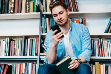 Hipster öğrenci okuma Halk Kütüphanesi elinde kitap ile oturan akıllı sms iletisi aldı. Genç adam cep telefonu cihaz 4 g internet bağlantısı kullanarak online sohbet