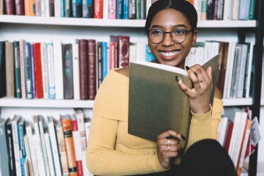 Elinde kitap uzağa arıyorsunuz ve holding ise vizyon düzeltme gülüyor için gözlük olumlu Afrikalı-Amerikalı genç kadın. Edebiyat Arsa bestseller dan zevk öğrenci neşeli koyu derili