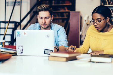 Online eğitsel Afro-Amerikan arkadaş aşağı vasıl okul sırası Kitaplığı'nda oturan ev ödevi yazma sırasında kablosuz Internet bağlantısı kullanarak modern dizüstü cihaz izlerken kulaklık dalgın genç adam
