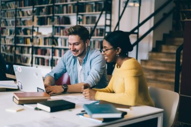 Neşeli çok kültürlü hipster öğrencilerin rahat giymek komik eğitsel bir modern dizüstü kablosuz 4 g kullanarak izlerken internet Kitaplığı'nda. Proje eğitim üzerinde teamworking farklı iki genç insanlar