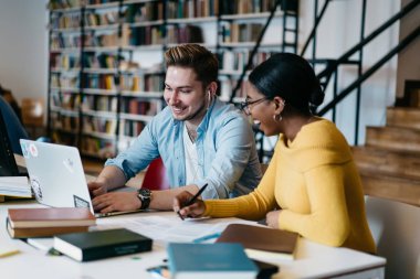 Webinar halk kütüphanesinde kablosuz Internet bağlantısı kullanarak modern dizüstü bilgisayarda izlerken gülmekten neşeli iki çok kültürlü öğrenci. Bilgi web sitelerinde arama olumlu çeşitli iş arkadaşları