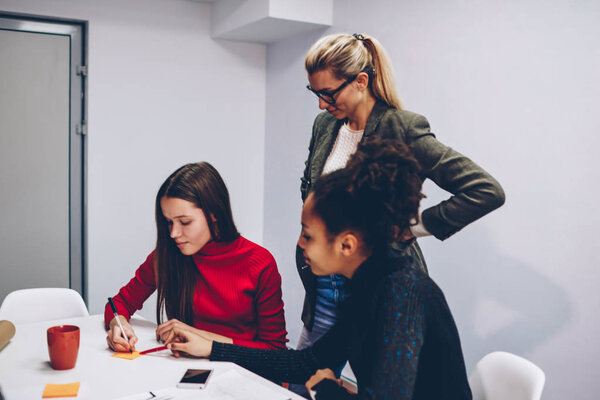 Young female students having lesson with coach in business school explaining information about startup planning, prosperous company owner controlling working process of employees making research