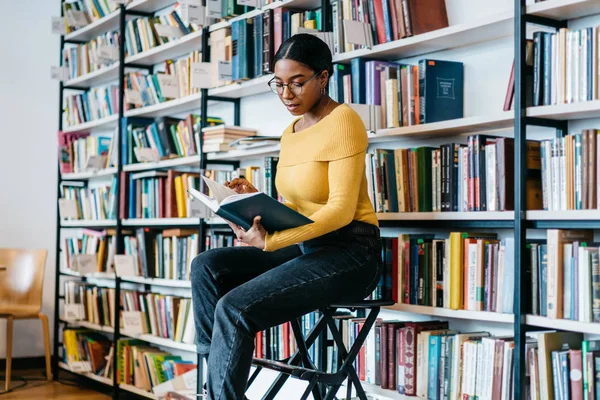 聚焦非洲裔美国年轻妇女在眼镜为视力矫正阅读文学书准备考试 沉思的深色皮肤学生在课程教科书中搜索信息 — 图库照片