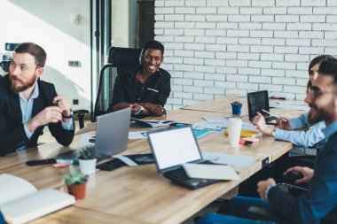 Çok kültürlü genç girişimciler iş karşılaşma içinde modern şirket sırasında gülüyor formal giyim giymiş. Pozitif çalışanların eğleniyor farklı takım office brifing sırasında masada oturan