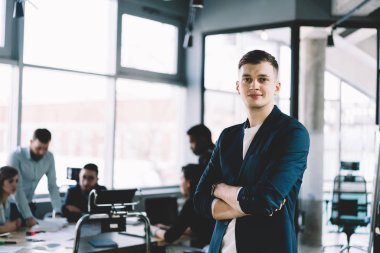Kamera arka planda office takımda çalışan meslektaşları süre bakarak çapraz elleriyle başarılı gurur CEO'su yarım uzunluk portre. Formal giyim tasarım şirketi olumlu erkek girişimci