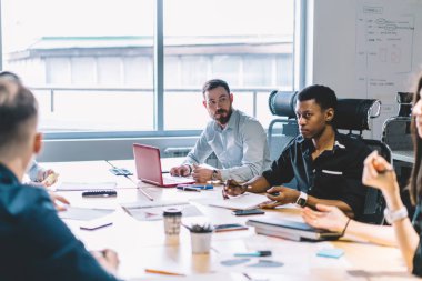 Formal giyim modern ofis dizüstü bilgisayarlar ile masada brifing sırasında yeni proje için fikirler tartışırken çalışanların takım giymiş. Çok kültürlü grup genç girişimcilerin iş toplantısı